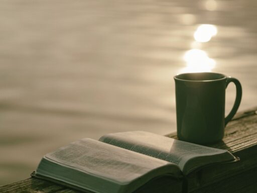 An open bible on a deck beside a cup of coffee.